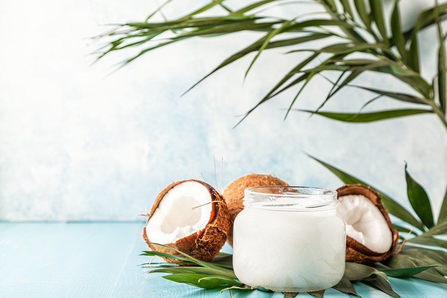 Coconut oil and coconuts on a bright pastel background, selective focus.