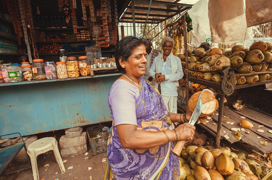 BELUR, INDIA - FEB 23, 2017: Street life and woman cutting coconut for milk near rustic store with food and snacks on February 23, 2017. Population of Karnataka state is 62000000 people